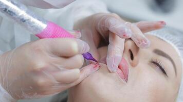 permanente lábio Maquiagem procedimento dentro progresso, fechar-se do uma esteticista usando tatuagem máquina, profissional Cuidado e estética para de longa duração lábio contorno video