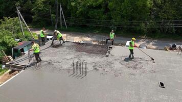 Construction workers pouring and leveling concrete slab. Aerial view of construction crew wearing safety vests as they pour, spread, and level wet concrete on a video
