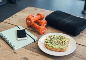 A plate of avocado toast, a towel and a pair of dumbbells on a wooden table photo