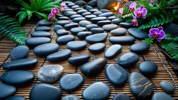 Smooth Black Stones Arranged on Bamboo Mat with Green Ferns photo