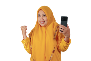 Middle aged woman in yellow hijab smiling and raising fist with smartphone in hand png