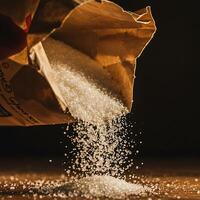 Pouring Granulated Sugar From Paper Bag on Wooden Surface photo