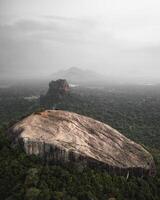 Aerial view Pidurangala Rock with Sigiriya Lion Rock in Central Province Sri Lanka surrounded by dense tropical forest and misty hills under cloudy dramatic sky photo