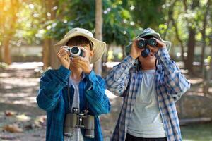 2 Asian boys use binoculars and a camera to study the local birds in a community forest. Soft and selective focus. photo