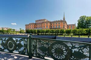 Mikhailovsky Castle is visible behind an openwork bridge fence and a river under a blue sky. photo