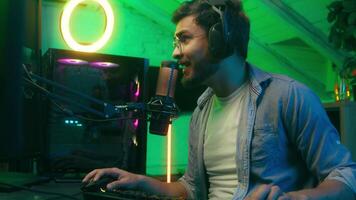 Emotional smiling talking in microphone game addict Caucasian guy male man streamer gamer wearing headphones playing virtual battle internet entertainment web online carefree computer at night video