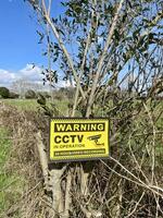 A yellow warning sign on a bush in a field photo