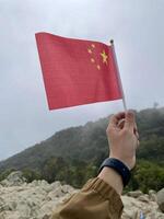 A person holding up a chinese flag on a rocky hill photo