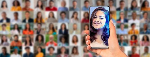 A person holds a smartphone that shows a facial recognition scan of their face. Behind them, a diverse crowd is visible, highlighting modern identification technology in action. photo