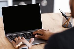 Unrecognizable black businessman typing on small modern laptop keyboard with empty screen, african american manager working online in his office, attending online webinar or making training, mockup photo
