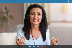 Conference. Portrait Of Senior Lady Wearing Headset Having Virtual Chat, Looking And Talking To Camera During Web Call, Explaining And Discussing Something In Headphones. Teleworking photo
