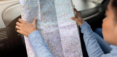 Using map in road trip for directions in new city at travel. Young serious attractive african american woman reading chart while sitting in car, planning route and exploring way, empty space, cropped photo