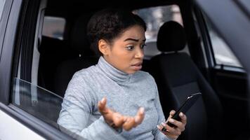 Travel problems and get lost in new city and looking for road, sitting in car. Upset confused excited young african american woman with map looks in smartphone and cannot find way, empty space photo