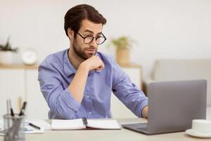 Surpirsed Business Guy In Eyewear Looking At Laptop Having Computer Problem Sitting At Desk In Modern Office. Issue With Internet Connection Concept. Selective Focus photo