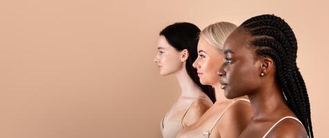 Profile Shot Of Three Beautiful Body Positive Multiracial Women. Side View Of Young Pretty Ladies With Different Skin Types And Appearances Posing Together Over Beige Studio Background, Free Space photo