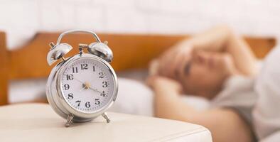 Insomnia problem. Senior woman lying in bed, woke up at 4 am, focus on alarm clock, panorama photo