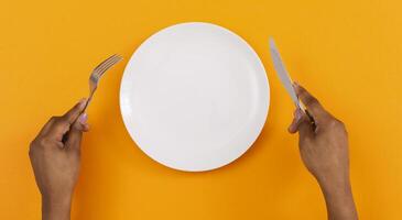 Lunch time. Top view of empty plate with fork and knife in black woman's hands on orange background, panorama photo