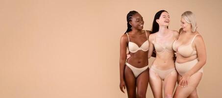Portrait Of Body Positive Women Of Different Nationalities And Weight Types Posing On Beige Background, Full Length Shot Of Beautiful Black Female, Plus Size Woman, And Lady With Vitiligo In Underwear photo