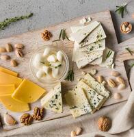 Assortment of cheese with nuts and rosmary on wooden board over grey concrete background, top view. photo