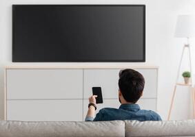 Modern gadgets. Unrecognizable man with smartphone connected to TV, watching at home, back view. Guy transfering from phone to television. Information transfer between devices over wifi. photo