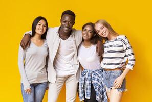 Positive multiethnic group of teenagers posing over yellow studio background photo