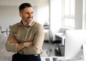 Happy middle aged businessman standing by his workplace, looking aside at copy space, thinking of new startup or project, smiling at good thoughts, planning investment, enjoying success photo