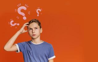 Thoughtful Caucasian teenager searching for creative solution to problem on orange background, collage with question marks. Copy space. Smart ideas and innovative decisions concept photo