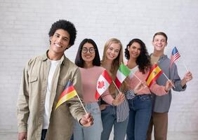 Modern education of international students or immigrants. Happy generation z multiracial people waving different countries flags at college classroom on white wall background, studio shot, empty space photo