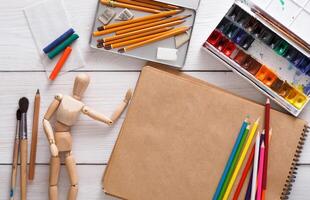 Workplace of artist. Paints, sketchbook and wooden painter man with brushes on white desk, top view, flat lay, objects photo