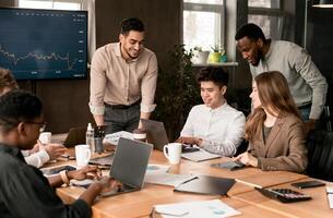 Teamwork, Lifestyle And Corporate Meeting Concept. Smiling Diverse Creative Group Working At Office, Having Breefing. Multiracial Colleagues Using Laptops, Looking At Screen, Making Project Together photo