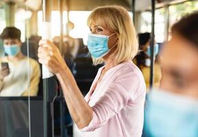 Safe Ride. Portrait of serious senior woman wearing protective face mask taking crowded bus holding handle, standing inside and looking out of window. Rush hour traffic, new normal life rules, covid photo