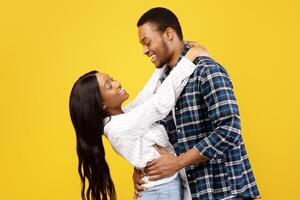 Free time, weekend, date and romance. Smiling young african american man and lady have fun, hug and look at each other, isolated on yellow background, studio shot, profile, copy space, cut out photo