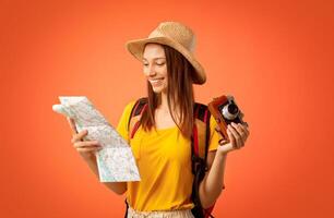 Happy girl traveller with camera looking at map, yellow studio background photo