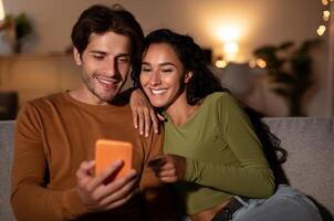 Cheerful Couple Using Cellphone With New Application, Wife Pointing Finger At Phone Browsing Internet Sitting On Couch At Home. Spouses Recommending Great App. Gadgets Concept photo