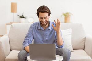Call. Man Waving Hand To Laptop Screen Communicating Online Sitting On Sofa At Home. Guy Gesturing Hello To Computer Having Conference. Modern Distant Communication Concept photo