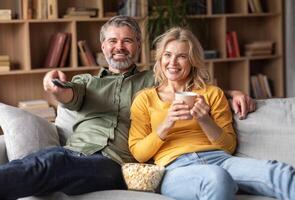 Home Relax. Happy Married Middle Aged Couple Watching Tv In Living Room, Smiling Spouses Eating Popcorn And Drinking Coffee Together While Relaxing On Comfortable Couch, Closeup Shot photo