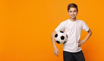 Young football player. Confident boy posing with soccer ball on orange studio background, panorama with copy space photo