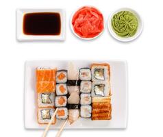Japanese food restaurant. Sushi set served on white platter with soy sauce, ginger, wasabi and chopsticks picking one piece. Top view, flat lay at white background with copy space photo