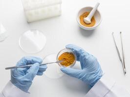 Quality control. Scientist hands taking turmeric or curcuma for analizing in the laboratory, white background photo