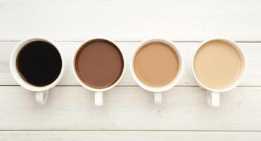 Different cups of coffee on white wooden table, top view. Gradient from light americano with milk to strong black espresso, copy space photo