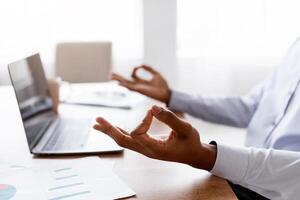 Closeup of Unrecognizable African American Businessman Meditating In Office In Front Of Laptop, Practicing Yoga At Work, Trying To Handle Stress About Deadline, free space, cropped photo