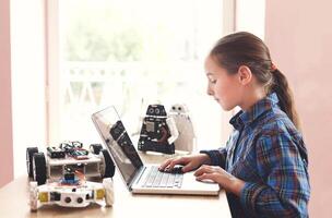 Creating robotics project, mockup. Concentrated girl typing the plan of innovation robot model in laptop, diy concept. Stem education. photo