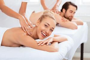 Couples Massage Therapy. Woman Smiling To Camera While Receiving Neck Massage During Relaxing Procedure At Spa Salon. Relaxation And Beauty Treatment For Two. Selective Focus photo