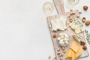 Set of cheese with nuts on wooden board and wine glasses over white concrete background, top view, copy space. Cheese and wine concept photo