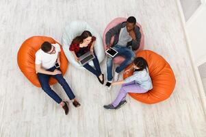 Group of young multiethnic friends using gadgets sitting indoors at university campus and working together on creative task, top view with copy space photo