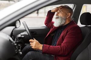 Shocked senior businessman having troubles on road, sitting in car, touching his head, side view, copy space. Astonished grey-haired aged man having car accident, suffering from stress photo