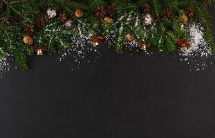 Christmas background with copy space, top view on pine tree twigs with pine cones, nuts and snow frame on black table. Xmas decorations, winter holidays concept photo