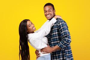 Rejoice together, date, funny dance and have fun. Millennial happy african american students husband and wife enjoying and hugging, isolated on yellow background, empty space, studio shot photo