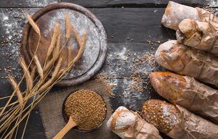 Bread background. Brown and white whole grain loaves wrapped in kraft paper composition on rustic dark wood with empty desk copy space. Baking and home bread making concept. Soft toning photo