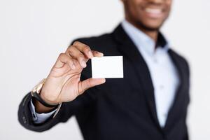 Business Card Mock-Up. Smiling black businessman holding blank card for clients or business partners, selective focus on empty white card, grey studio background, closeup, copy space photo